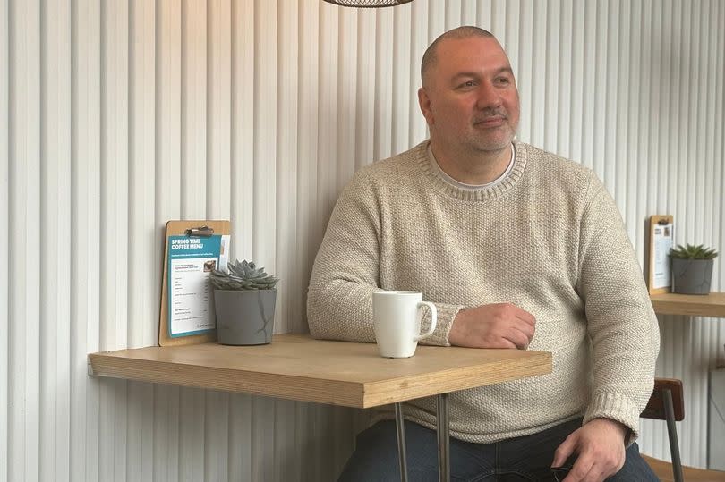 Man sitting by table with coffee cup, in the café at Tramshed Tech Cardiff. Jaymie Thomas is the founder of AI Wales J