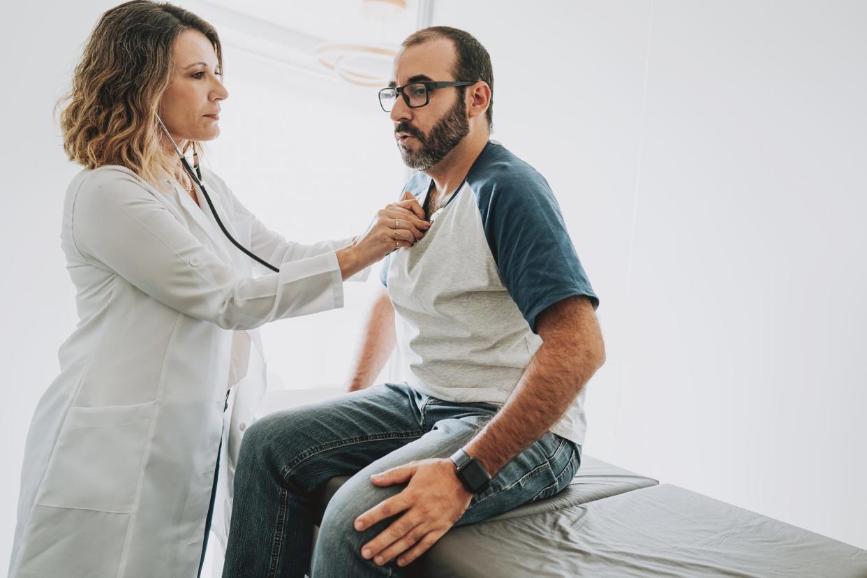 A female doctor listening to the heartbeat of a male patient.