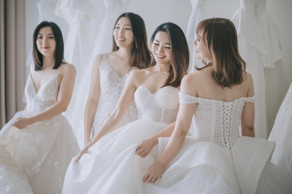 Bridesmaids in elegant wedding dresses with intricate lace and tulle details smile and pose together.