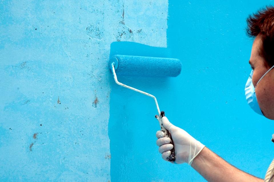 a man wearing a mask uses a roller to paint a wall blue