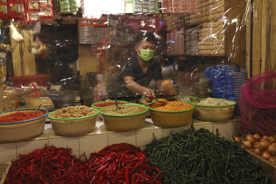 A spice vendor wearing a face mask waits for customers behind a protective plastic sheet at a traditional market in Tangerang, Indonesia, Saturday, May 9, 2020. (AP Photo/Tatan Syuflana)
