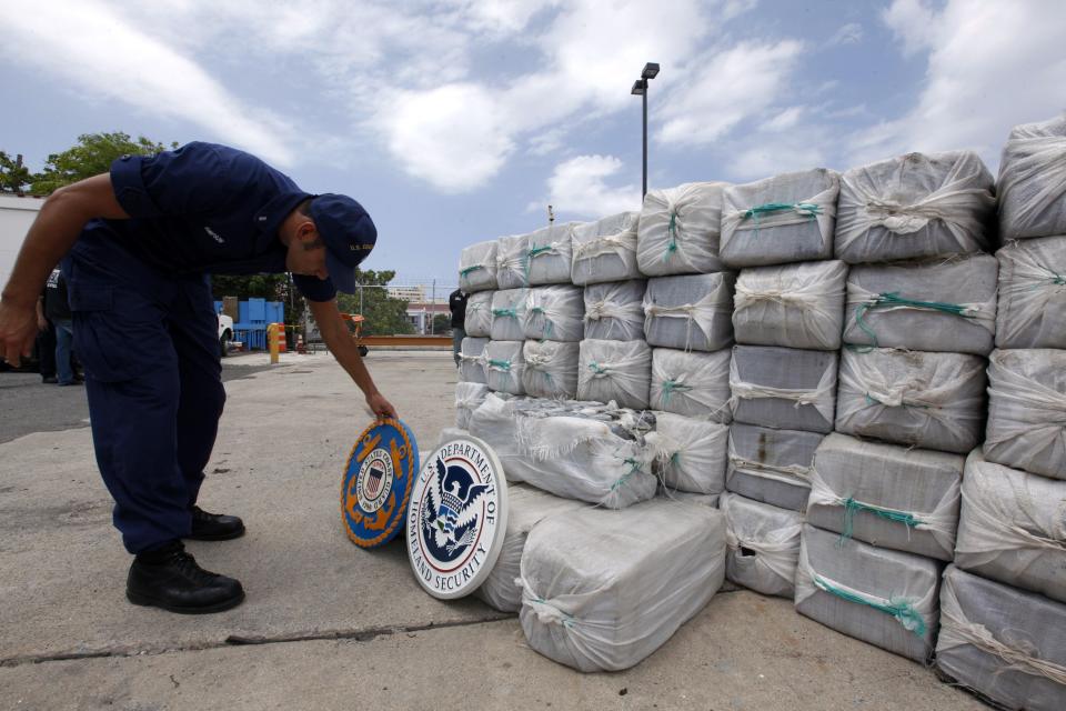 A U.S. Coast Guard adjusts the U.S. Coast Guard emblem in front of bags of cocaine seized in a routine patrol during a media presentation in San Juan, May 6, 2014. The U.S. Coast Guard recovered 1280 kg (2822 pounds) of cocaine, worth an estimated $37 million, on April 29 during an at-sea interdiction south of Puerto Rico and also arrested two traffickers from the Dominican Republic. REUTERS/Ana Martinez (PUERTO RICO - Tags: CRIME LAW DRUGS SOCIETY)