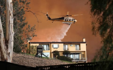 A Los Angeles County Fire Department helicopter makes a water drop on flames behind a home in Malibu, California - Credit: AP