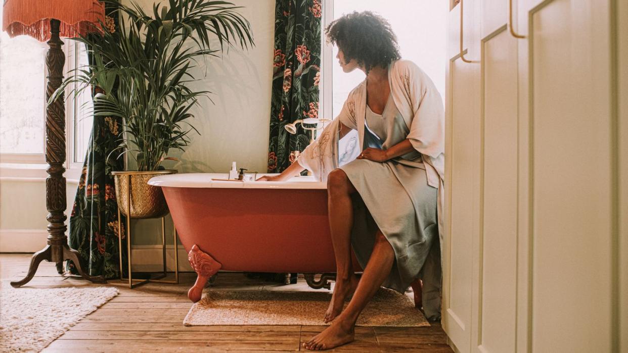 dreamy scene of a beautiful woman perching on the side of a roll top bathtub in a luxurious room