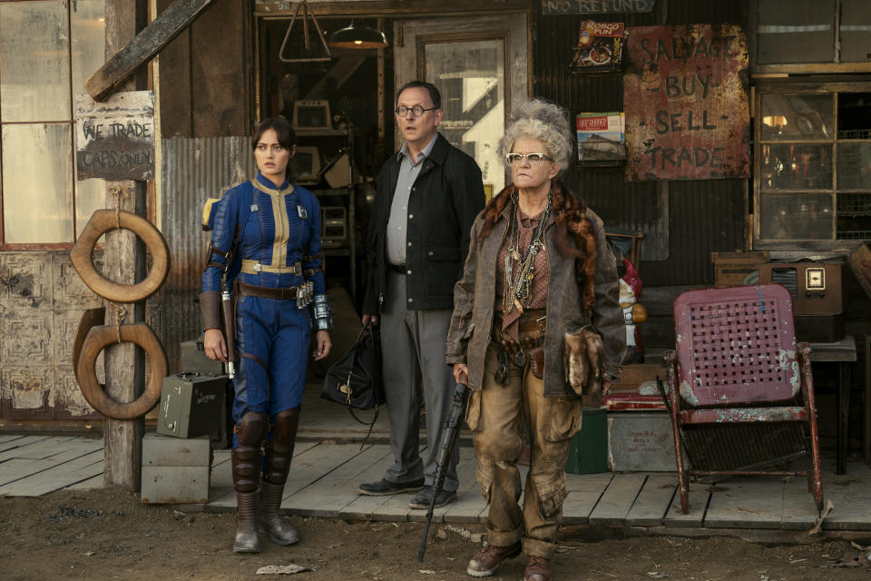 three people (Ella Purnell as Lucy MacLean, Michael Emerson as Wilzig, and Dale Dickey as Ma June) stand in front of a dilapidated store, in 'Fallout'