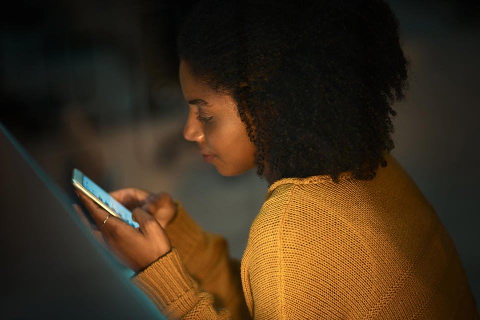 Shot of a young designer using a cellphone while working in an office at night