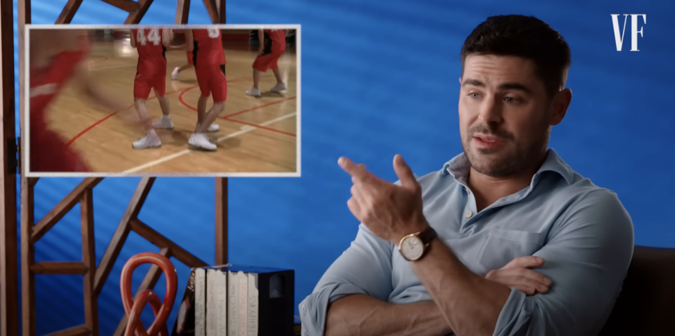 Zac Efron discusses a scene from a basketball game shown in an inset. He's seated, wearing a light shirt, pointing to the inset image. Vanity Fair logo present