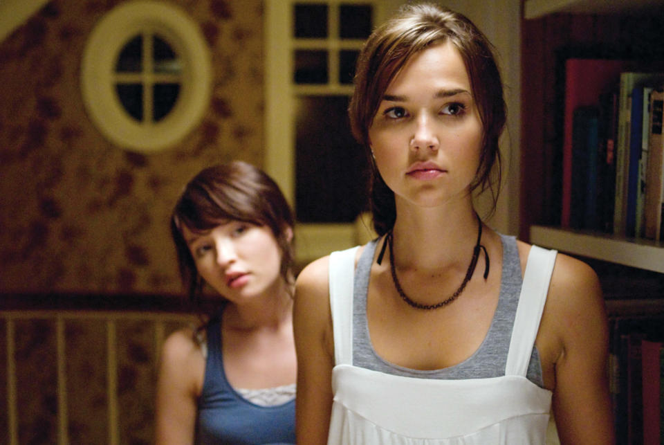 Two girls standing by a bookshelf looking at something