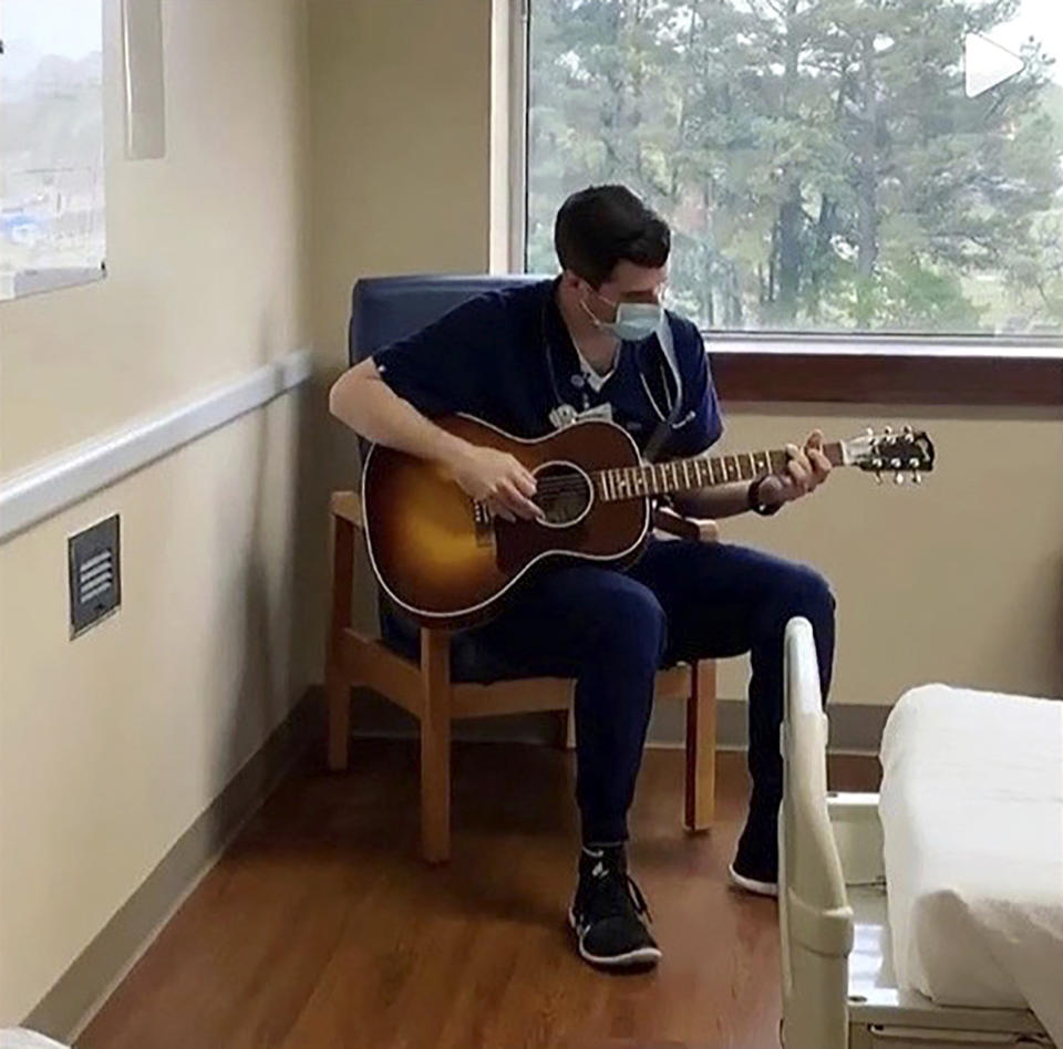 In this March 2020 image taken from video provided by Adam Blackerby, Michael Stramiello plays the guitar inside a hospital room in Benton, Ark. In a time of anxiety and isolation, simple acts of kindness from hospital workers are giving comfort to patients and their families. Stramiello plays and sings for stressed-out staffers and patients. (Adam Blackerby via AP)