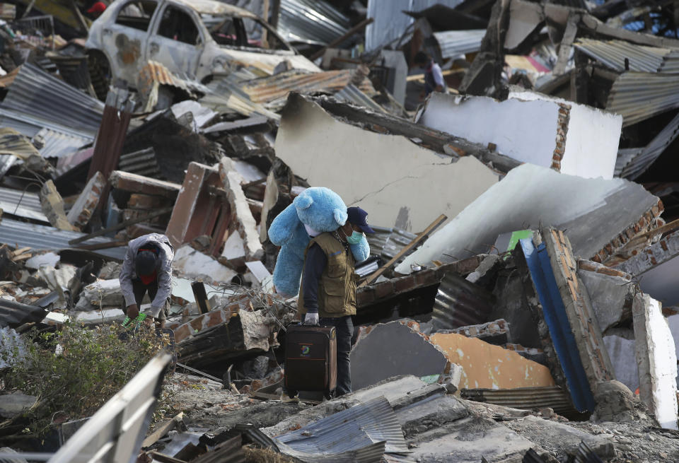 In this Saturday, Oct. 6, 2018, file photo, a man carries a teddy bear and other items he recovered from his toppled house at the earthquake-hit Balaroa neighborhood in Palu, Central Sulawesi, Indonesia. (AP Photo/Aaron Favila, File)