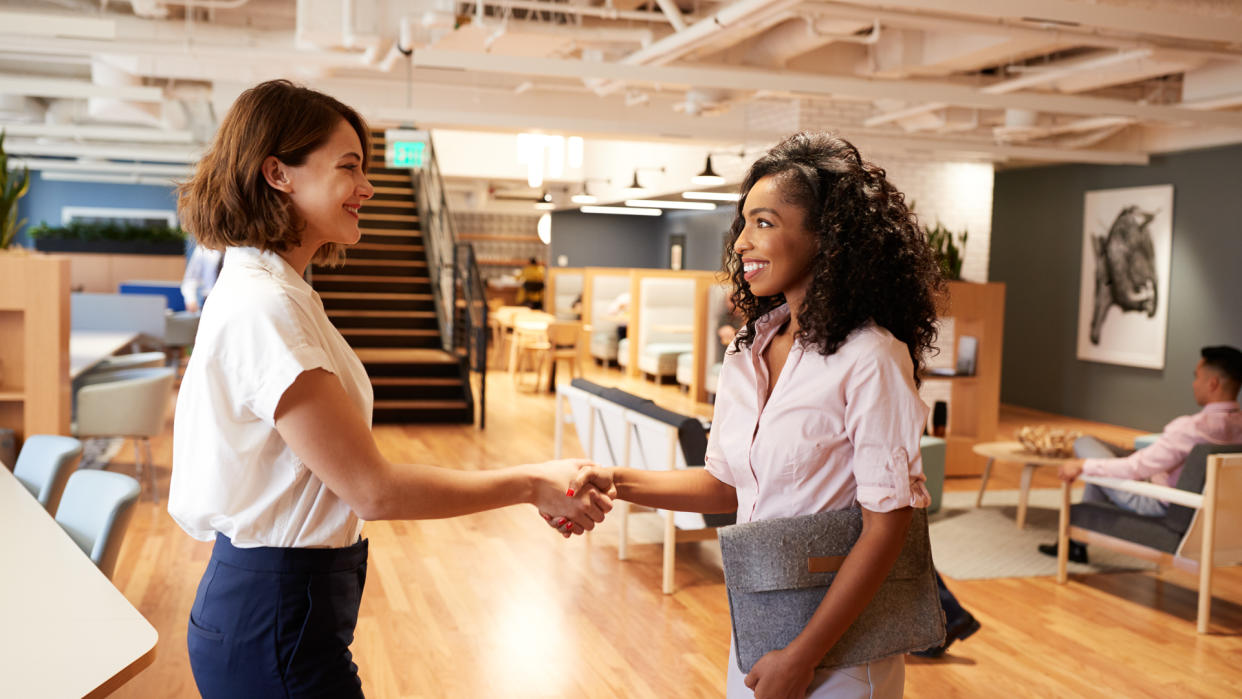 Two Businesswomen Meeting And Shaking Hands In Modern Open Plan Office.