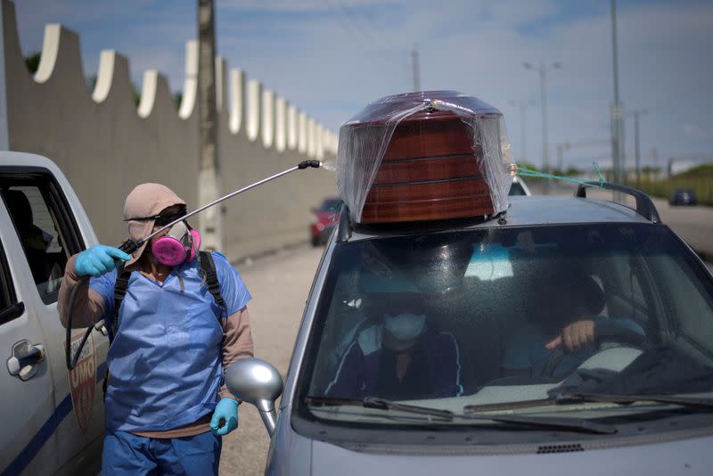 A worker sprays disinfectant on a vehicle carrying a coffin lined up to enter a cemetery as Ecuador's government announced on Thursday it was building a "special camp" in Guayaquil for coronavirus disease (COVID-19) victims, in Guayaquil