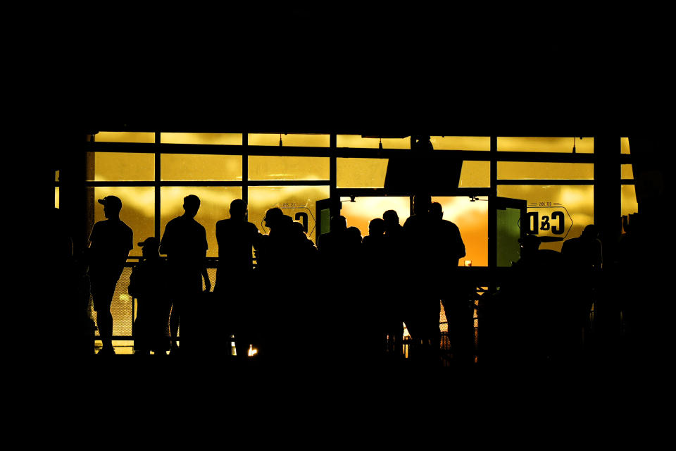 Fans are silhouetted by the setting sun as the watch from a club during the fourth inning of a baseball game between the Kansas City Royals and the Tampa Bay Rays Thursday, July 4, 2024, in Kansas City, Mo. (AP Photo/Charlie Riedel)