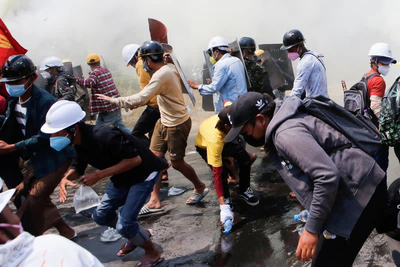 Tear gas and fire extinguisher gas float around demonstrators as they run away from police during a protest against the military coup in Naypyitaw