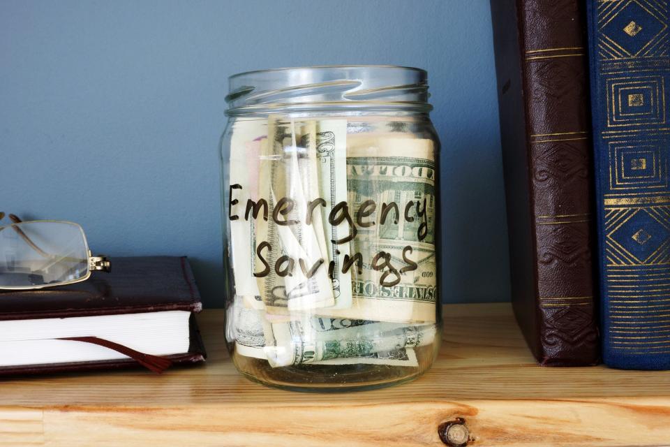 A jar that says emergency savings is on a bookshelf and full of cash.
