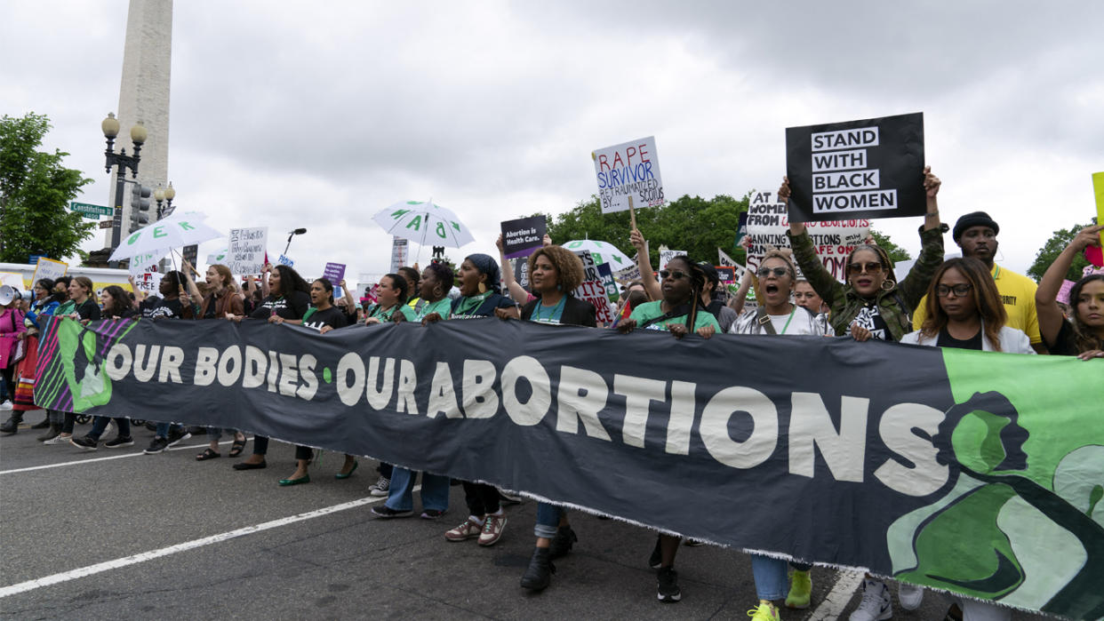 Demonstrators chant as they jointly hold a huge banner saying: Our Bodies, Our Abortions, as well as signs saying: Stand With Black Women, Rape Survivor Re-traumatized by ... SCOTUS, and so on. and others.