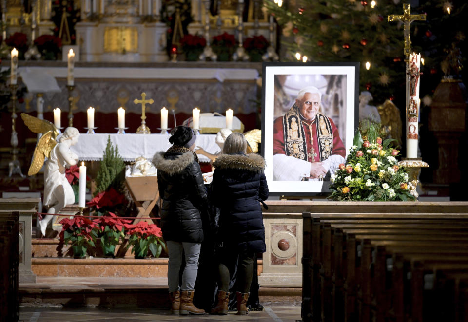 Two persons stay in front of a portrait of Pope Emeritus Benedict XVI at the Saint Magdalena church in Altoetting, Germany, Saturday, Dec. 31, 2022. Pope Emeritus Benedict XVI, the German theologian who will be remembered as the first pope in 600 years to resign, has died, the Vatican announced Saturday. He was 95. (AP Photo/Andreas Schaad)