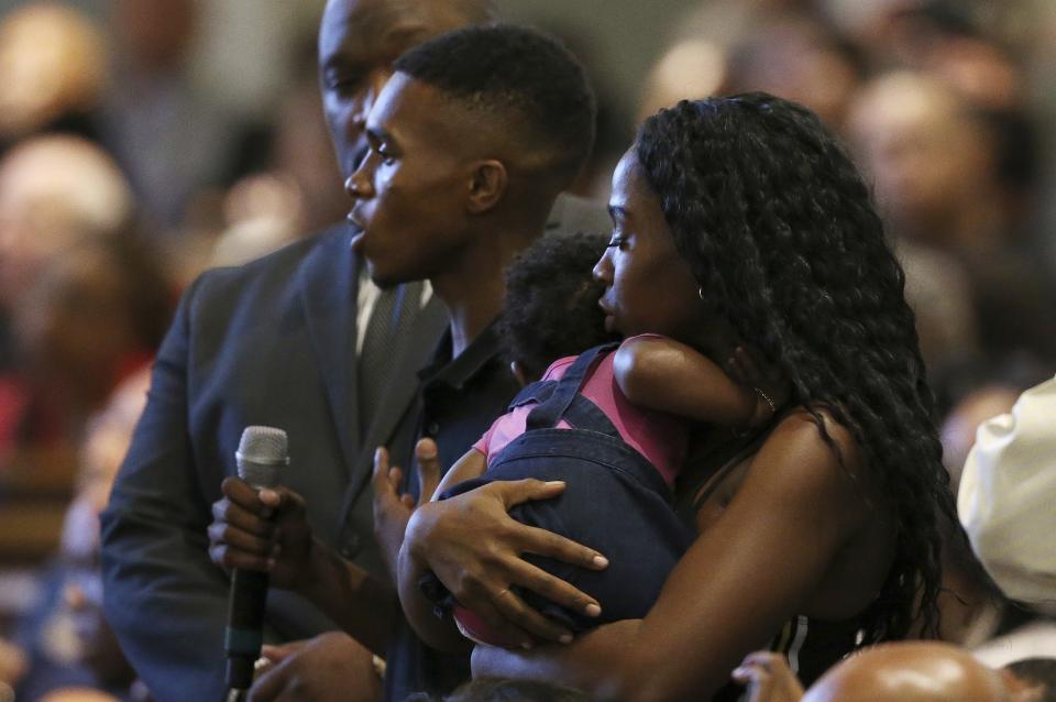 FILE - In this June 18, 2019 file photo Dravon Ames, holding microphone, speaks to Phoenix Police Chief Jeri Williams and Phoenix Mayor Kate Gallego, as his fiancee, Iesha Harper, right, holds 1-year-old daughter London, at a community meeting in Phoenix. Still stinging from national outrage sparked this summer by a videotaped encounter of officers pointing guns and cursing at the family, community members are holding low-key meetings aimed at helping Phoenix officials figure out how citizens could help oversee the city's officers. (AP Photo/Ross D. Franklin, File)