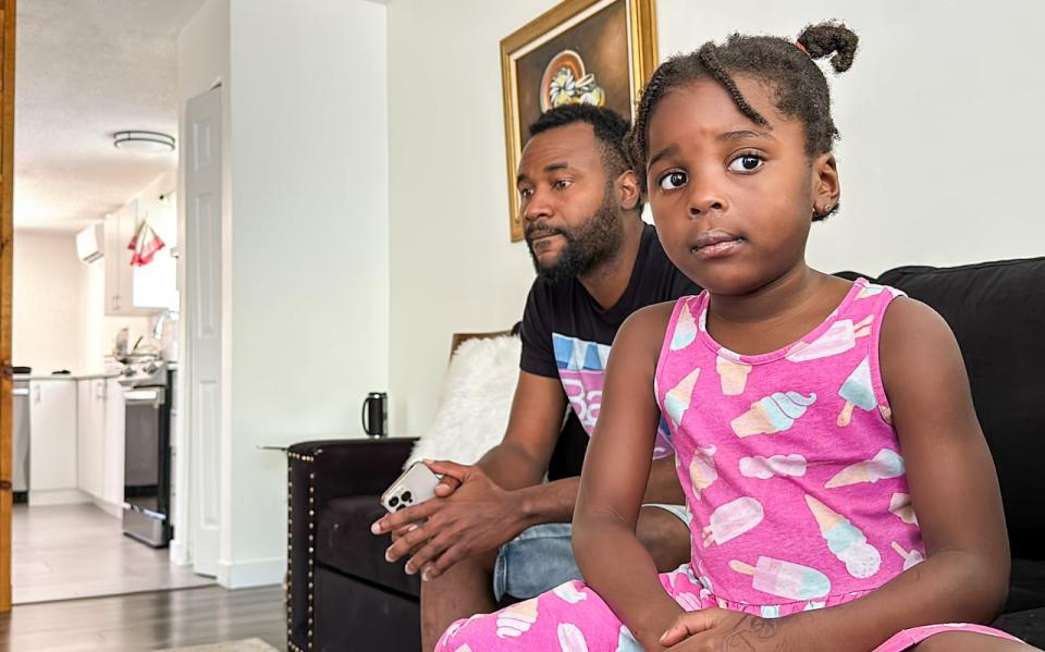 Junot Raphael sits with his daughter at their home in Gatineau's Buckingham sector. Raphael took a job driving for a mysterious package delivery company near Ottawa's airport and spent weeks waiting to get paid.