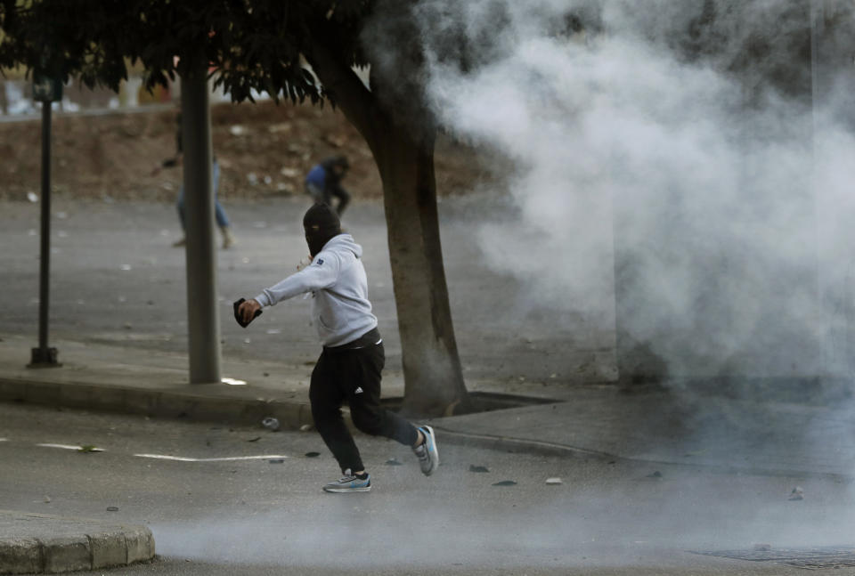 A supporter of the Shiite Hezbollah and Amal Movement groups, throws stones against the riot policemen, as they try to attack the anti-government protesters squares, in downtown Beirut, Lebanon, Saturday, Dec. 14, 2019. Lebanon has been facing its worst economic crisis in decades, amid nationwide protests that began on Oct. 17 against the ruling political class which demonstrators accuse of mismanagement and corruption. (AP Photo/Hussein Malla)