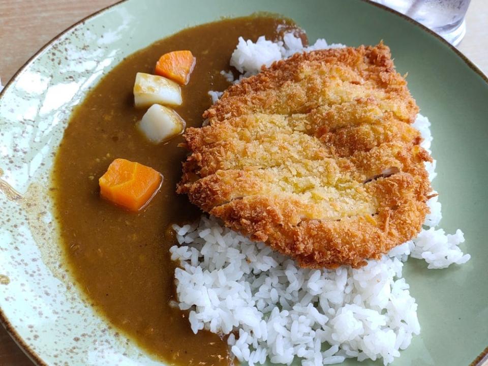 crispy chicken katsu cutlet on bed of white rice next to brown curry sauce with carrot pieces in it on green plate