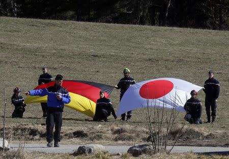 French rescue workers hold Germany's and Japan's flags during a ceremony in tribute to the Japanese victims at the memorial for the victims of the air disaster in the village of Le Vernet, near the crash site of the Germanwings Airbus A320 in French Alps, March 29, 2015. REUTERS/Jean-Paul Pelissier