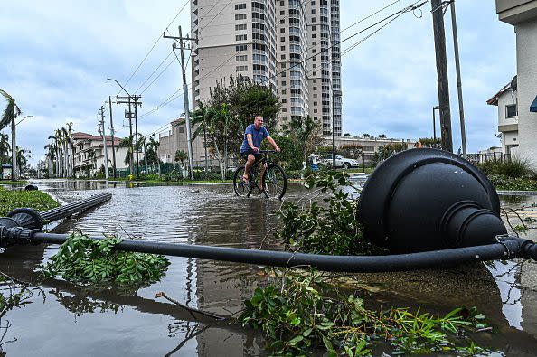 A man cycles through water past a downed street lamp in the aftermath of Hurricane Ian in Fort Myers, Florida, on September 29, 2022. - Hurricane Ian left much of coastal southwest Florida in darkness early on Thursday, bringing 