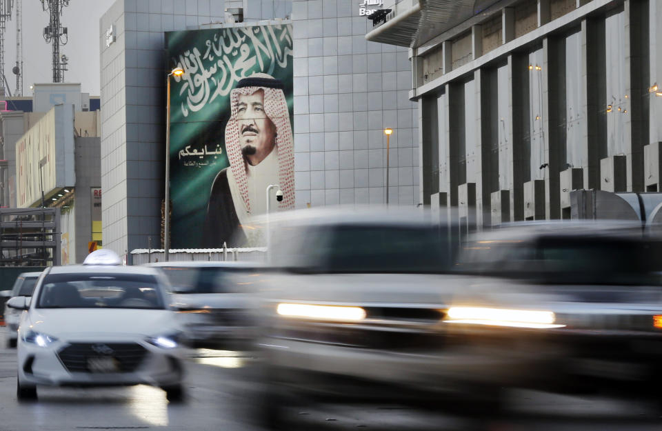 In this picture taken with low shutter speed, vehicles passes in front of a banner showing Saudi King Salman, with Arabic that reads "We pledge you to listen and obey" at a shopping mall, in Riyadh, Saudi Arabia, Thursday, Sept. 19, 2019. Any attack on Iran by the U.S. or Saudi Arabia will spark an "all-out war," Tehran's top diplomat warned Thursday, raising the stakes as Washington and Riyadh weigh a response to a drone-and-missile strike on the kingdom's oil industry that shook global energy markets. (AP Photo/Amr Nabil)