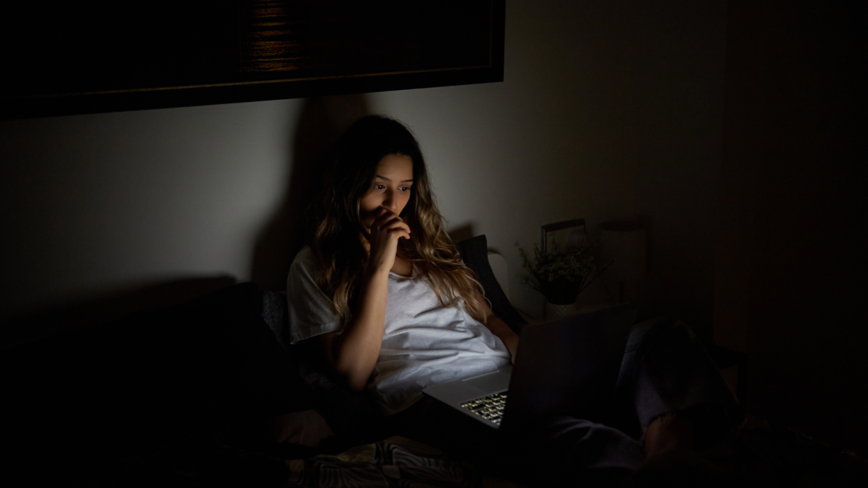 A woman using her laptop in bed late to represent doing late night online shopping.