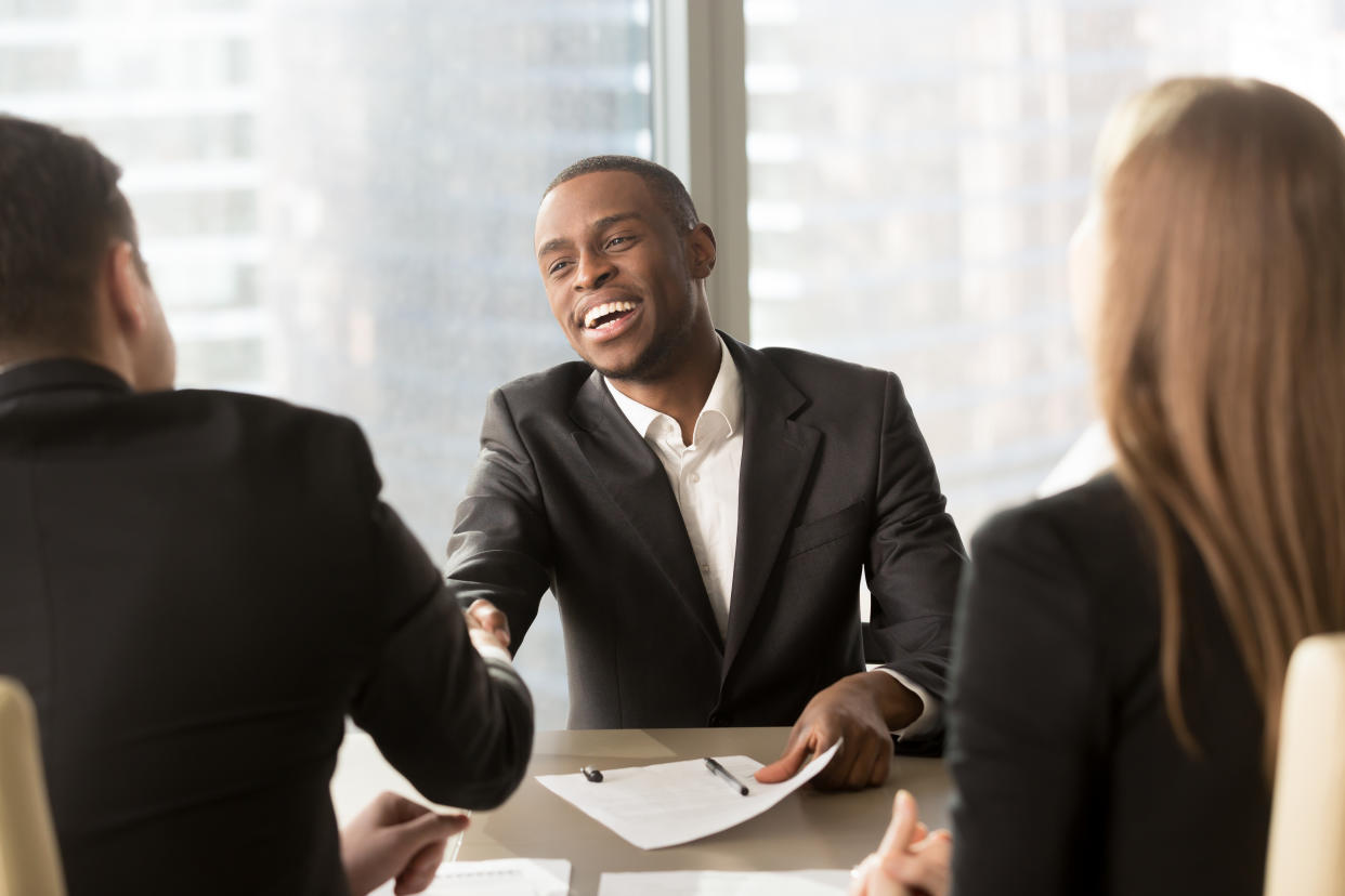 Excited smiling black businessman handshaking white partner at meeting, successful african applicant getting hired, got a job, satisfied multiracial businessmen shaking hands after signing document