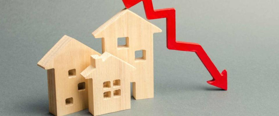 Miniature wooden houses and a red arrow down arrow, representing falling mortgage rates.