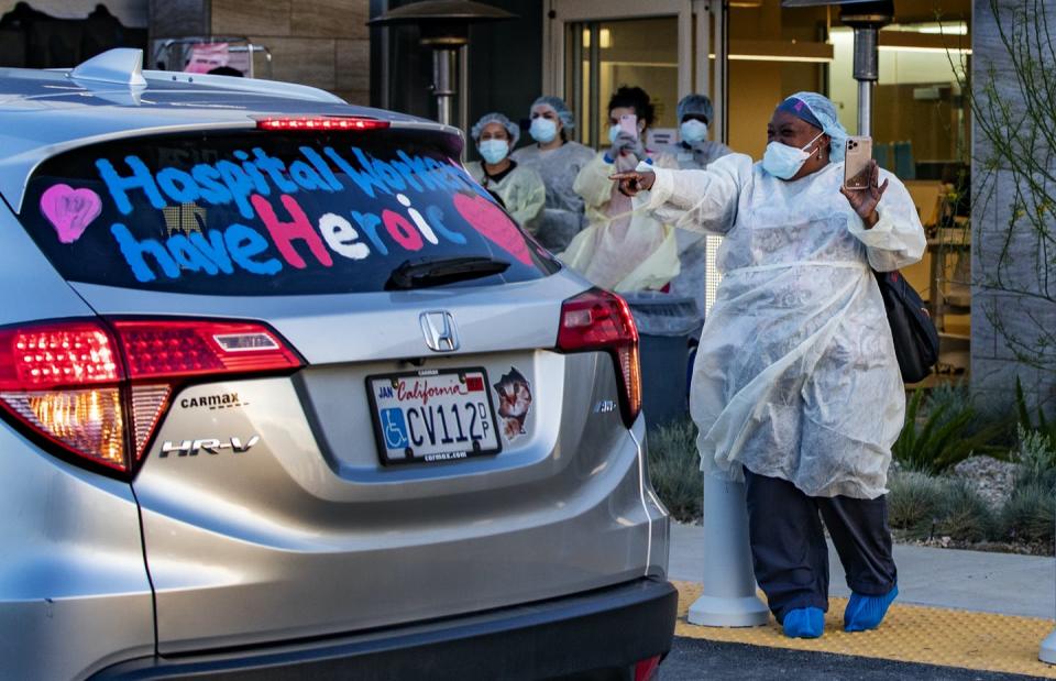 Women in surgical scrubs gesture at a car bearing the message hospital workers have heroic hearts