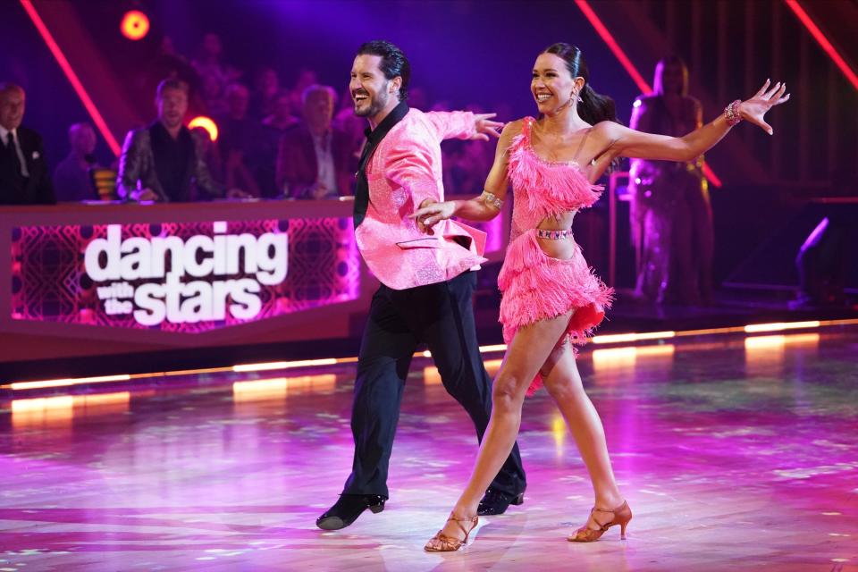 Two dancers perform on stage with smiles, man in a satin jacket and woman in a fringed outfit. The "Dancing with the Stars" logo is visible