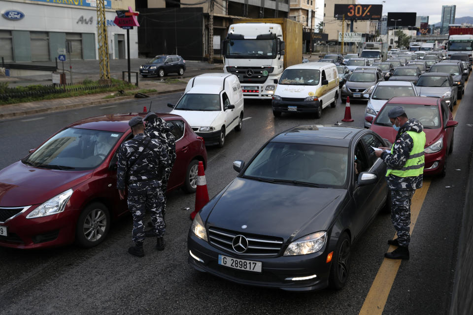 Police officers stand at a checkpoint to inspect cars that violate the lockdown, in Beirut, Lebanon, Thursday, Jan. 14, 2021. Lebanese authorities began enforcing an 11-day nationwide shutdown and round the clock curfew Thursday, hoping to limit the spread of coronavirus infections spinning out of control after the holiday period. (AP Photo/Bilal Hussein)