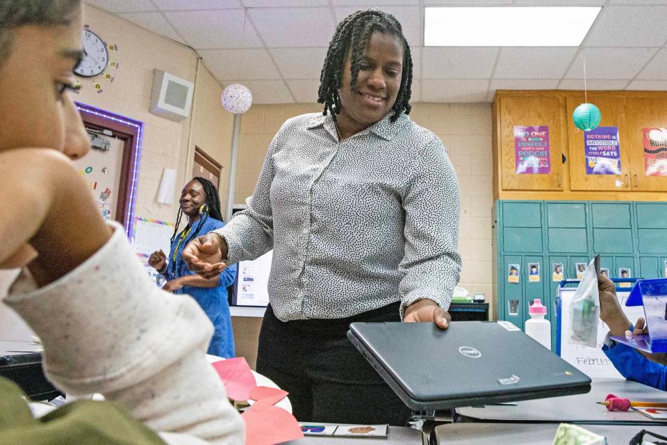 Paraprofessional Tameka Mays hands out a computer to a student of class N-1 at George Read Middle School in New Castle, Tuesday, Feb. 20, 2024