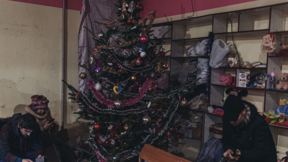 Una mujer y dos hombre en un refugio junto a un arbol de Navidad.