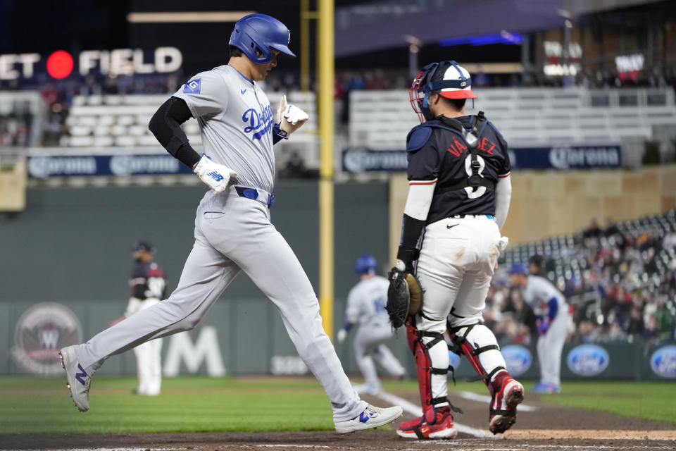 Los Angeles Dodgers designated hitter Shohei Ohtani, left, crosses home plate to score off an RBI single by Freddie Freeman during the sixth inning of a baseball game against the Minnesota Twins, Monday, April 8, 2024, in Minneapolis. (AP Photo/Abbie Parr)