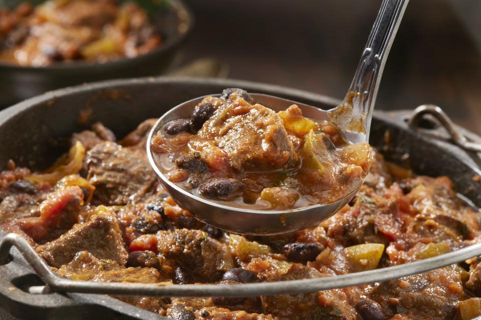 A ladle holds some chili above a simmering pot full of food.