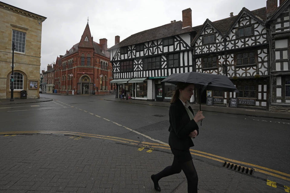 A woman walks alone a street in Stratford-upon-Avon, Warwickshire, England, Tuesday, Feb. 28, 2023. The foyer of the Other Place theater in Shakespeare's birthplace of Stratford-upon-Avon is a cozy refuge from winter. One day a week the theater becomes a "warm hub," set up by the Royal Shakespeare Company to welcome people who may be struggling to heat their homes because of sky-high energy prices. (AP Photo/Kin Cheung)