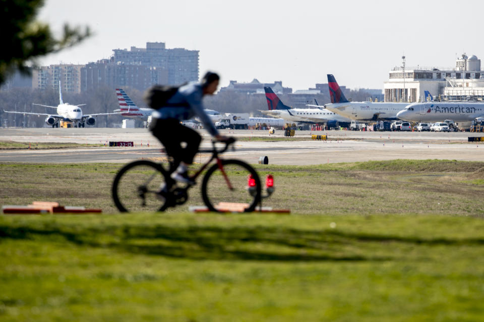 A bicyclist moves through Gravelly Point as planes arrive and depart at Ronald Reagan Washington National Airport, Monday, March 16, 2020, in Arlington, Va. (AP Photo/Andrew Harnik)