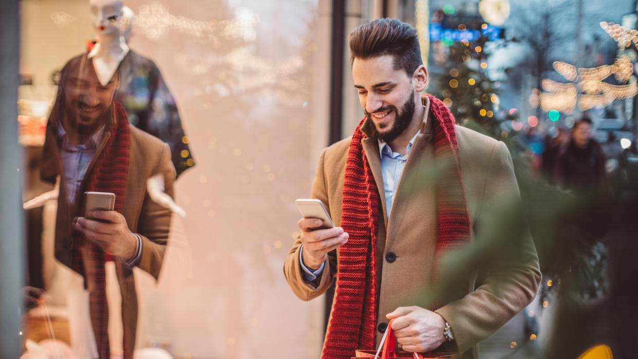 Young man holding  Christmas bags and checking his smart phone.