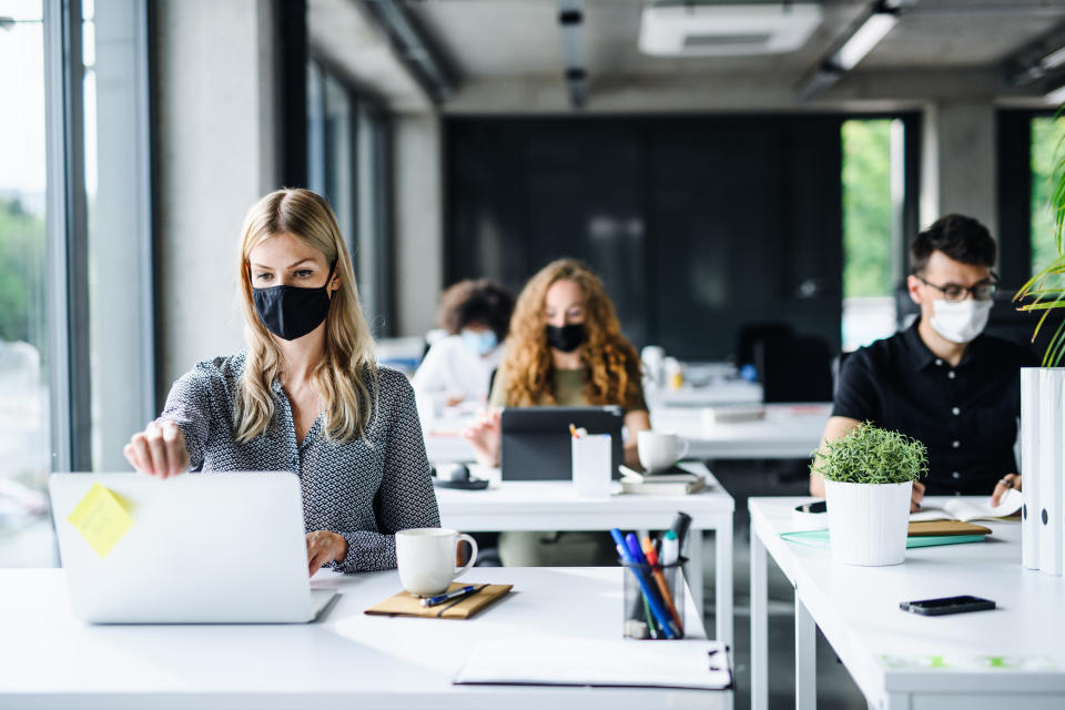 Young people with face masks back at work in office after coronavirus quarantine and lockdown.