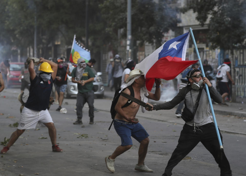 Protesters clash with the police in Santiago, Chile, Friday, Dec. 20, 2019. Chile marks a second full month of unprecedented social revolt that has not only altered the country's political landscape but also prompted a referendum on reforming the country's dictatorship-era. (AP Photo/Fernando Llano)