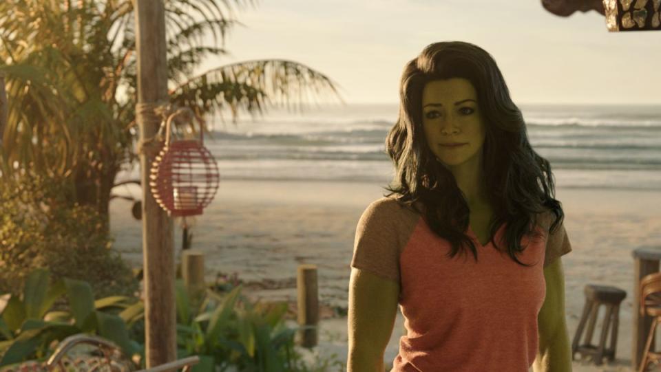 jennifer walters as she-hulk looks off camera while standing on a beach with the sun setting 