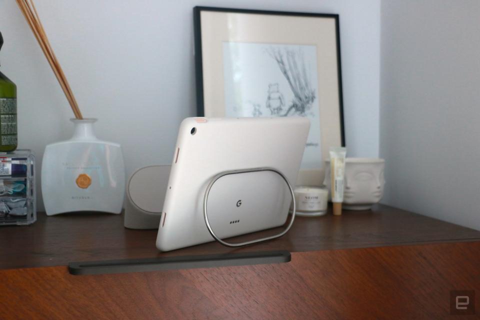 The Pixel Tablet on a walnut dresser propped up by the silver kickstand on the back of its protective case. 