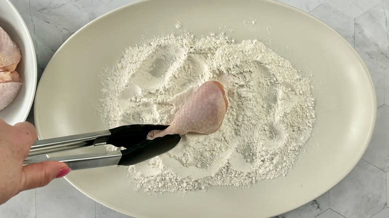 hand dipping chicken into flour