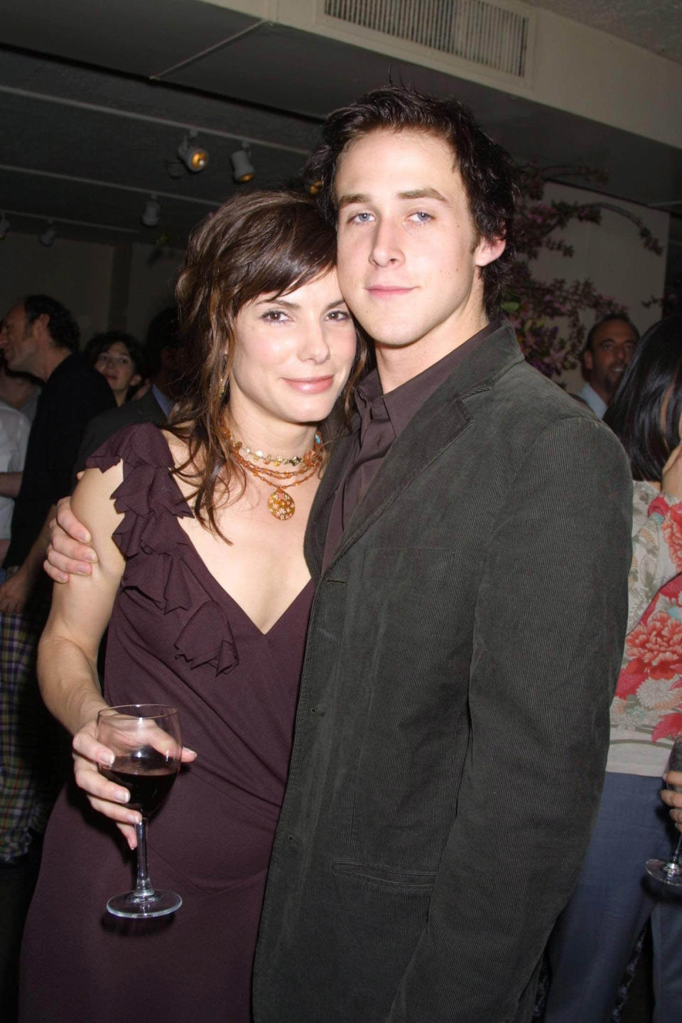 Sandra Bullock holding a wine glass and Ryan Gosling in a jacket putting his arm around her at the Murder by Numbers after party