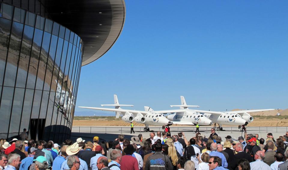 FILE - In this Oct. 17, 2011, file photo a crowd gathers outside Spaceport America for a dedication ceremony as Virgin Galactic's mothership WhiteKnightTwo sits on the tarmac near Upham, N.M. British billionaire Richard Branson is taking another concrete step toward offering rides into the close reaches of space for paying passengers. Branson announced Friday, May 10, 2019, that Virgin Galactic will immediately begin shifting operations from California to a spaceport and specialized runway in the New Mexico desert in final preparations for commercial flights. He says Virgin Galactic's development and testing program has advanced enough to make the move, which will continue through the summer. (AP Photo/Susan Montoya Bryan, File)