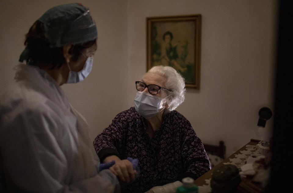 Pepita Jove Puiggros, 92, holds the hand of home care nurse Laura Valdes during a visit in Barcelona, Spain, April 2, 2020. Puiggros lives alone and receives food deliveries from a social service agency three days a week, but the deliveries have become more unpredictable amid the coronavirus pandemic. (AP Photo/Emilio Morenatti)