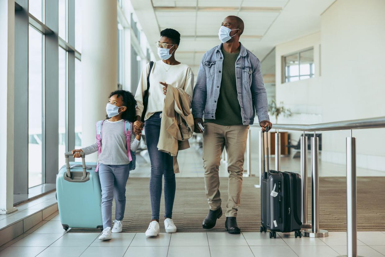 Tourist family walking through passageway in airport. Young girl with family in face masks walking with luggage in airport corridor.